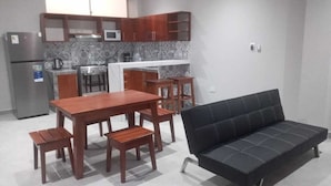 Un espace de vie compact comprenant un coin cuisine, une table à manger avec quatre chaises et un canapé noir.