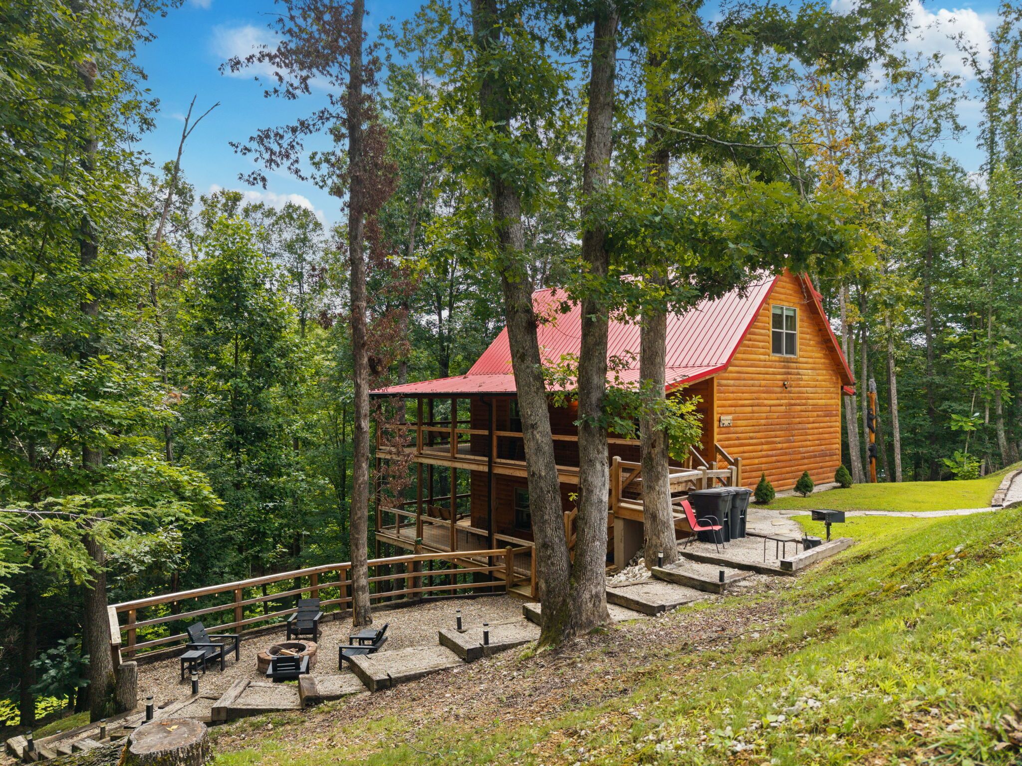 A wooden cabin with a red roof, surrounded by trees, and a deck with outdoor seating.