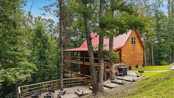A wooden cabin with a red roof, surrounded by trees, and a deck with outdoor seating.