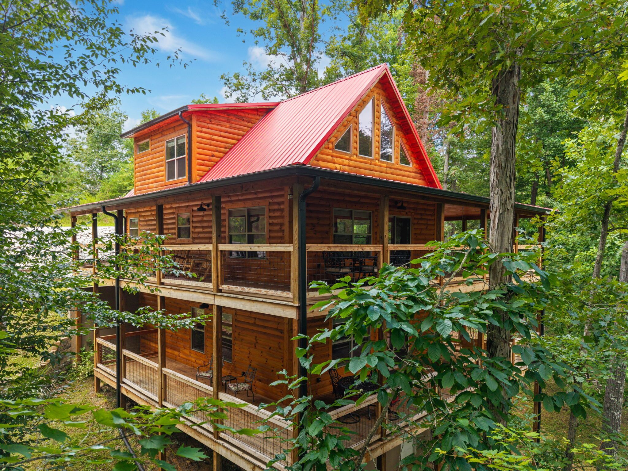A two-story log cabin with a red roof, surrounded by trees.