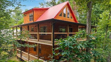 A two-story log cabin with a red roof, surrounded by trees.