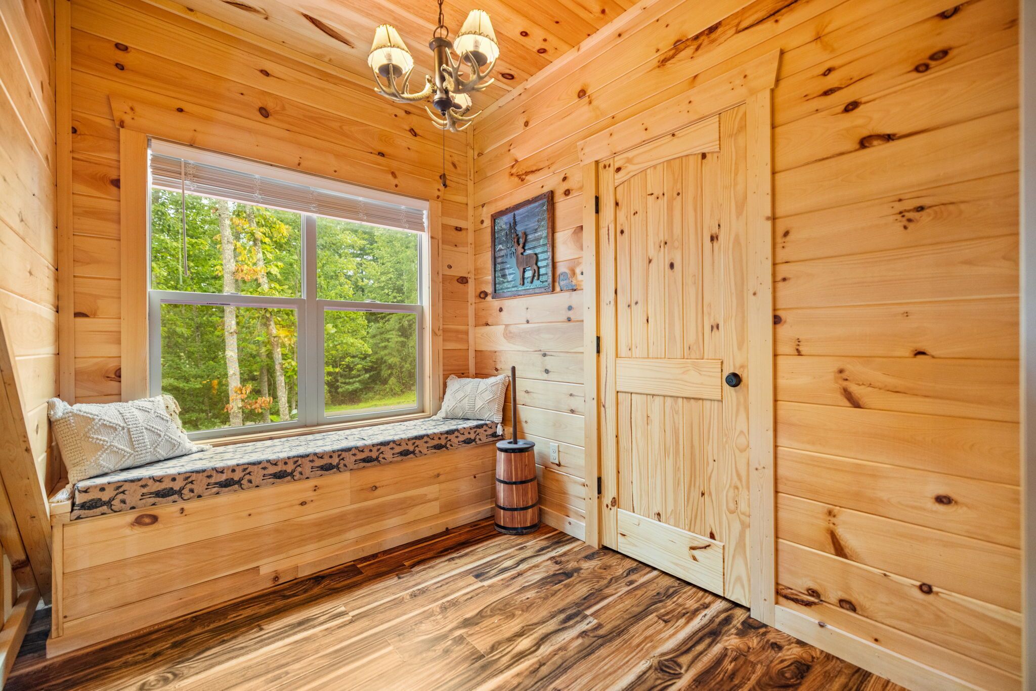 A cabin interior with a window seat, a door, and a wooden floor.