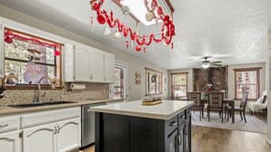 A kitchen with white cabinets, a central island, and a dining area with a table and chairs. - Spacious Mountain Retreat with Decks & Hot Tub in Kachina Village! (Flagstaff)