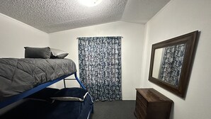 Opiskelija-asuntotyylinen huone, jossa on kerrossängyt, lipasto, kehystetty kuva ja kuviollinen verho.