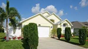A single-story house with a white garage door, a front yard with trimmed hedges, and a clear blue sky. - Maya Beautiful 4 BR Home 10 Minutes to Disney (Kissimmee)