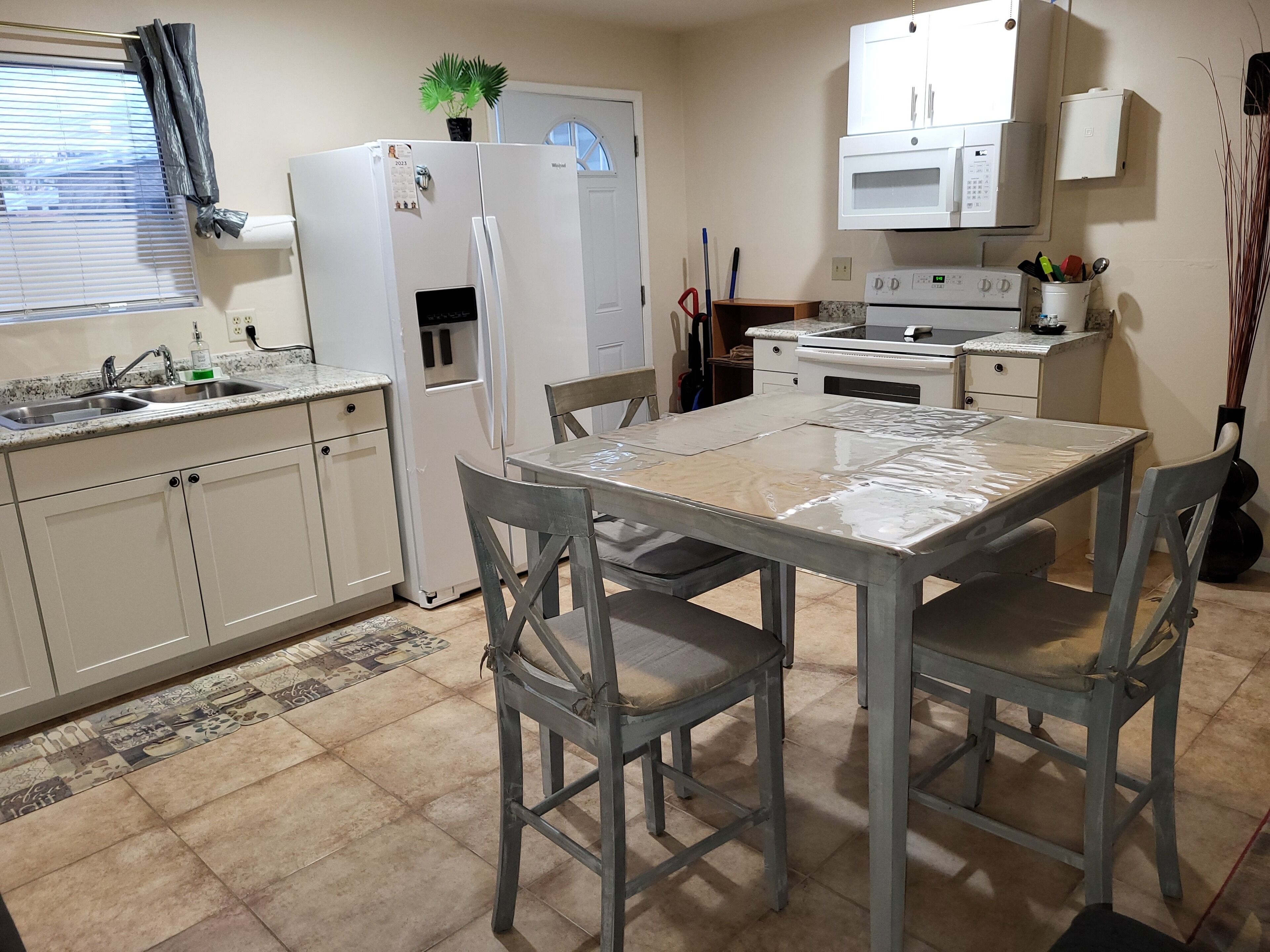 A compact kitchen with white cabinets, a refrigerator, a microwave, and a dining table with chairs.