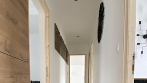 Ein Korridor mit Holzboden, weißen Wänden und Blick in einen Raum mit einem Bett.