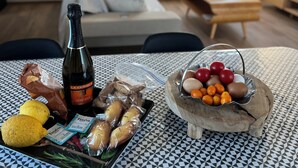 Ein Esstisch mit Speisen, einer Weinflasche und Blick auf ein modernes Wohnzimmer mit einer Couch und einem Fernseher.