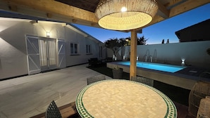 Eine überdachte Terrasse im Freien mit Pool, Tisch mit Stühlen und einer hängenden Lampe.
