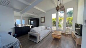 A modern living space with a sofa, a dining table, and a TV. There is a kitchen area with cabinets and a countertop. - Maison Récente Avec Piscine Privée à 300m de la mer (Lucciana)
