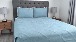 A modern bedroom with a grey upholstered headboard, a light blue quilted bedspread, and two bedside tables with lamps. - Luxury 2 Bed 1Bath Monthly. (Las Vegas)