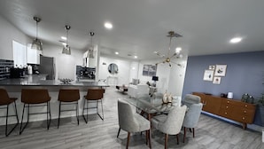 A modern kitchen with a central island, bar stools, and a dining area with a glass table and chairs. - Luxury 2 Bed 1Bath Monthly. (Las Vegas)