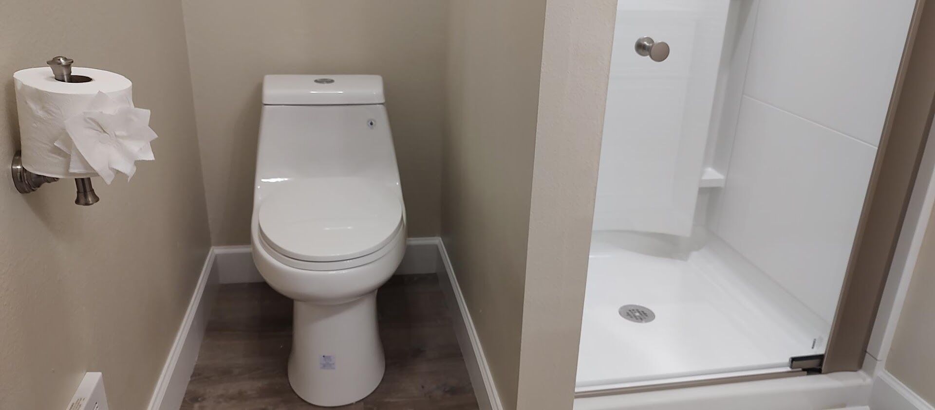 A bathroom with a toilet, a shower, and a toilet paper holder.