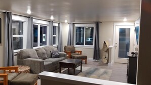 A living room with a grey sofa, a wooden coffee table, and a TV mounted on the wall.