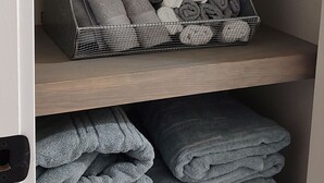 A storage unit with shelves holding rolled towels and a painting of a sunset over a marina.