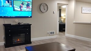 A living room with a fireplace, a flat-screen TV mounted on the wall, and a clock on the wall.
