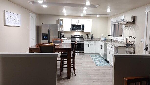 A modern kitchen with white cabinets, stainless steel appliances, and a dining area with wooden chairs and a table.