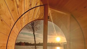 A wooden cabin with a circular window overlooking a lake at sunset.