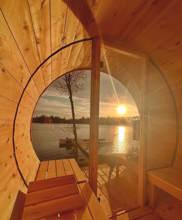 Una cabaña de madera con un ventanal circular que da a un lago al atardecer.