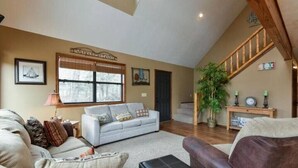 A living room with a sofa, a coffee table, a staircase, and a large window. - Lakefront 5 Bedroom, 3 Bath Cabin on Tablerock Lake, PONTOON available to rent! (Eagle Rock)