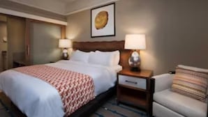 Hotelkamer met een groot bed, twee nachtkastjes met lampen, een kleine zithoek en een kunstwerk aan de muur.