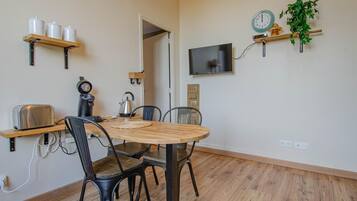 Eine kleine Küche mit Holztisch, Stühlen, einem Toaster, einem Wasserkocher und einer Uhr an der Wand.