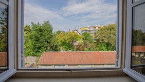 A view through a window of a building with a red-tiled roof, surrounded by trees and other buildings. - L'Idéal - SAINTE SAVINE (SAINTE SAVINE)