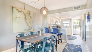 A dining area with a wooden table and blue chairs, a map on the wall, and a kitchen in the background.