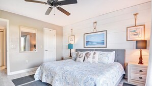 A bedroom with a bed, a nightstand, a ceiling fan, a framed picture, and a door.