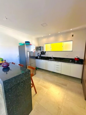 Una cocina moderna con armarios blancos, encimera negra y pared amarilla.