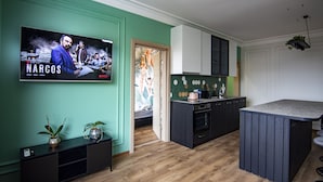Una cocina moderna con una televisión mostrando un programa, suelo de madera y una pequeña isla.