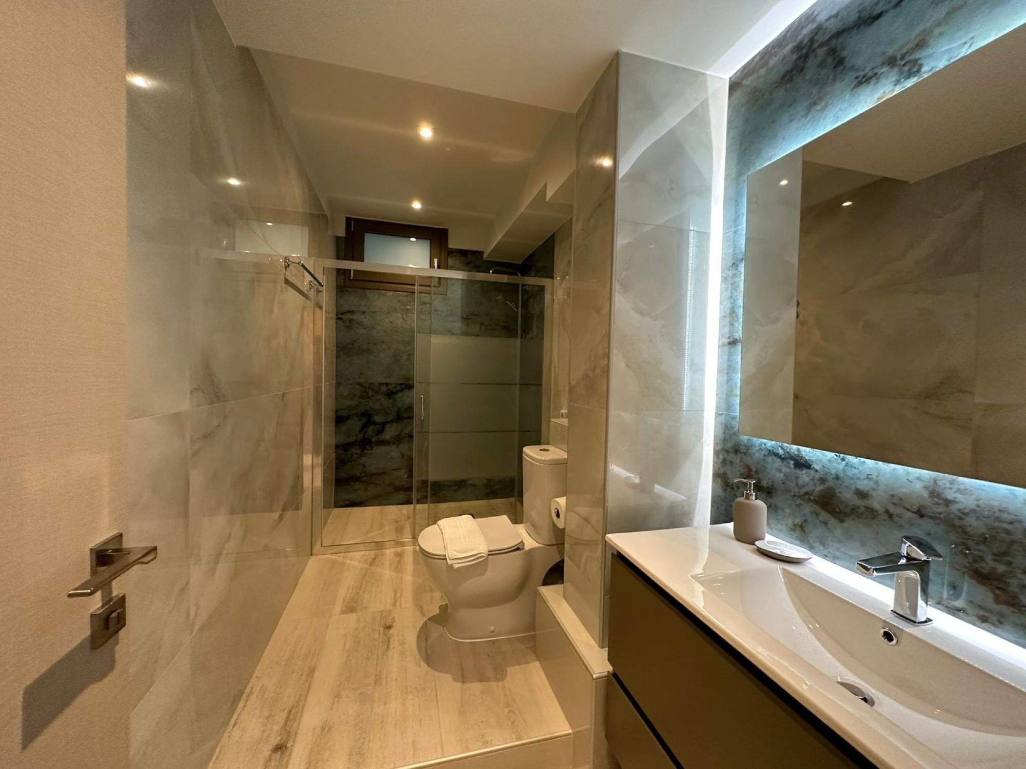 A modern bathroom with a glass-enclosed shower, a toilet, and a vanity with a marble countertop and a large mirror.
