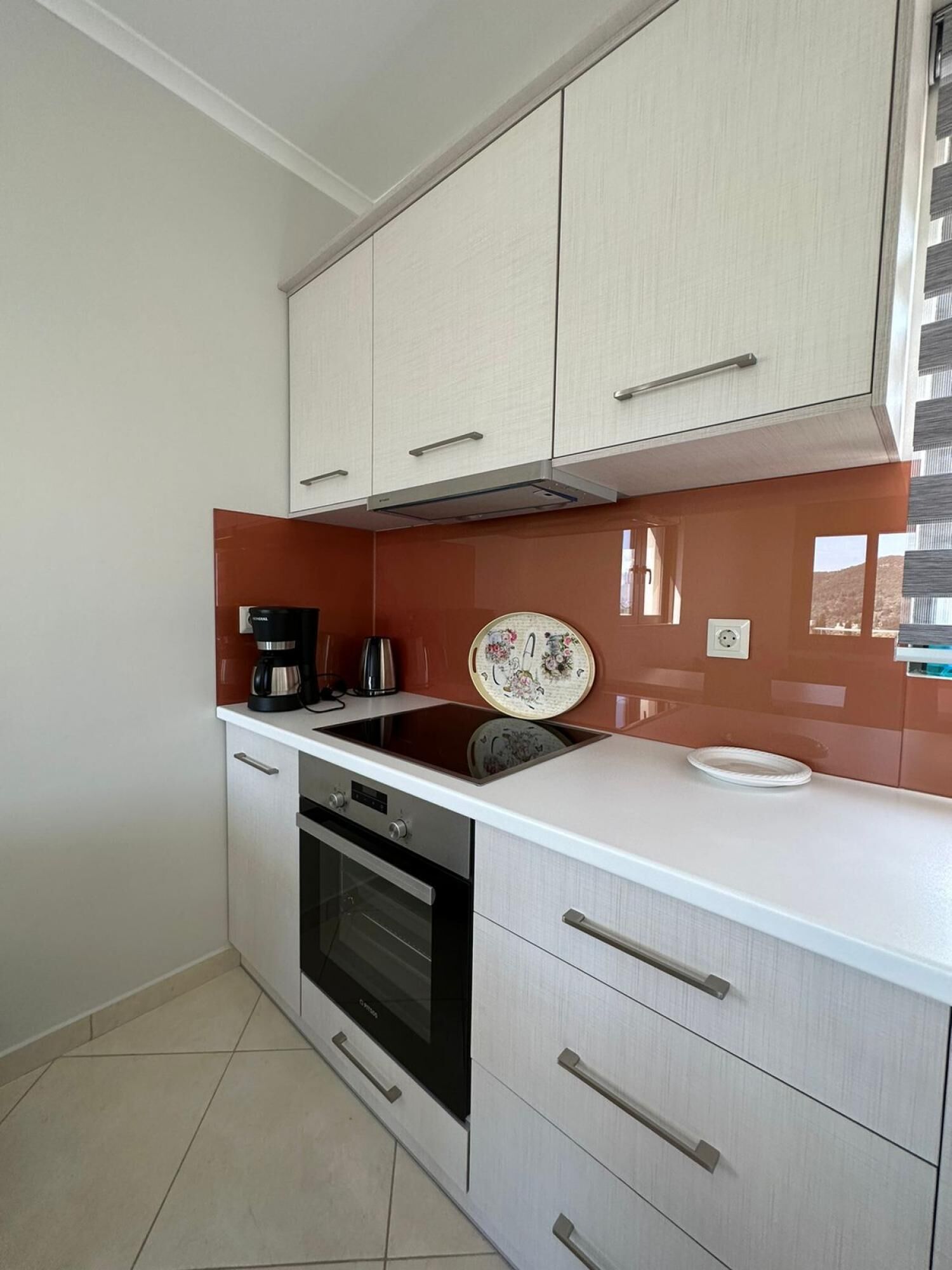 A compact kitchen with white cabinets, a built-in oven, and a coffee maker.