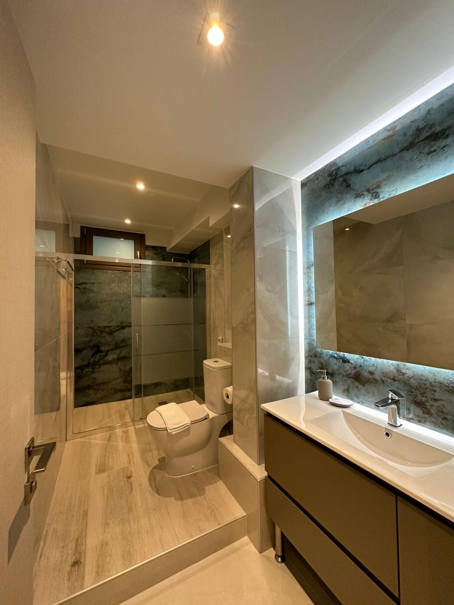A modern bathroom with a glass-enclosed shower, a toilet, and a vanity with a large mirror.