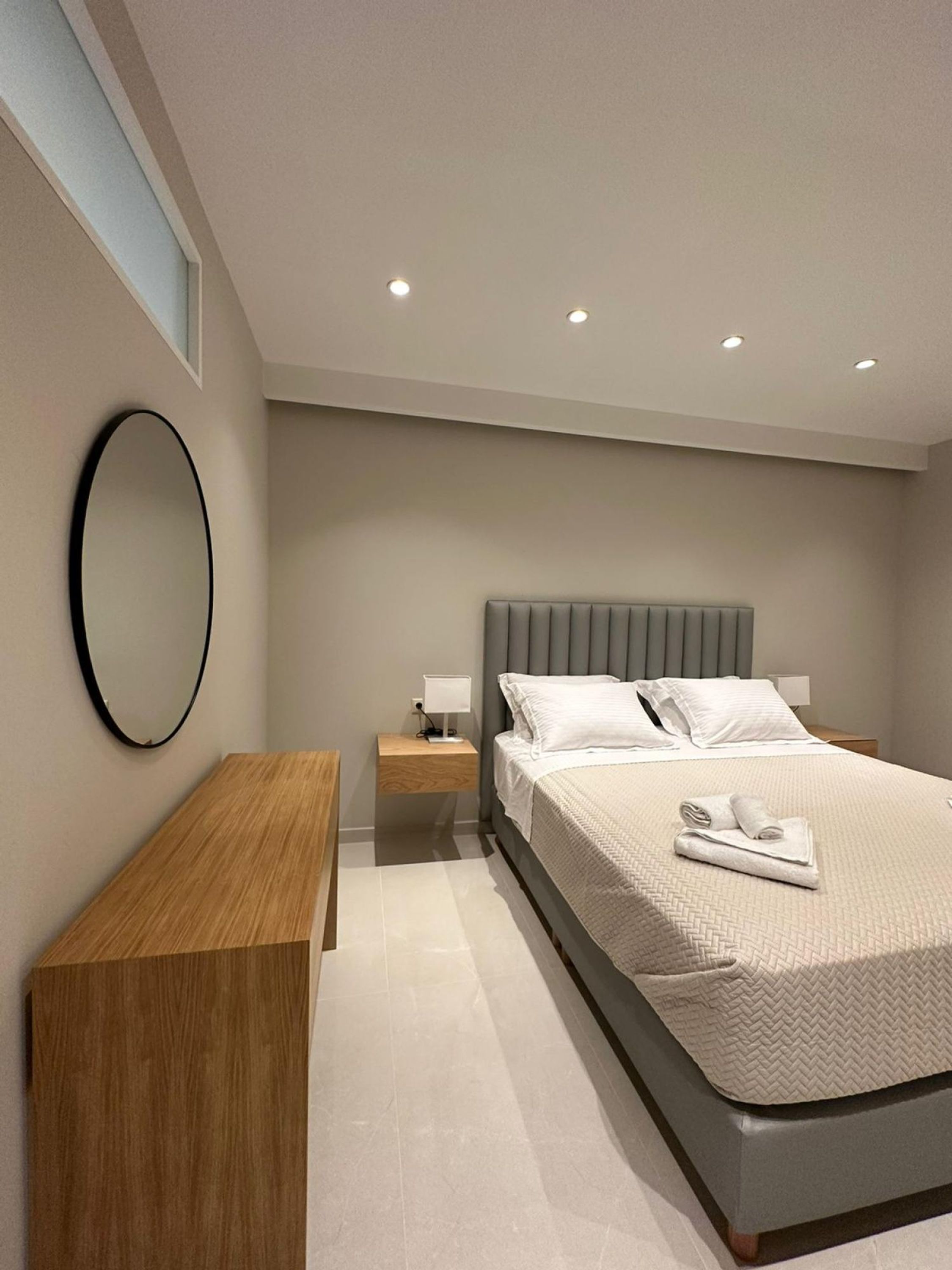 A modern bedroom with a bed, bedside tables, a mirror, and recessed ceiling lights.
