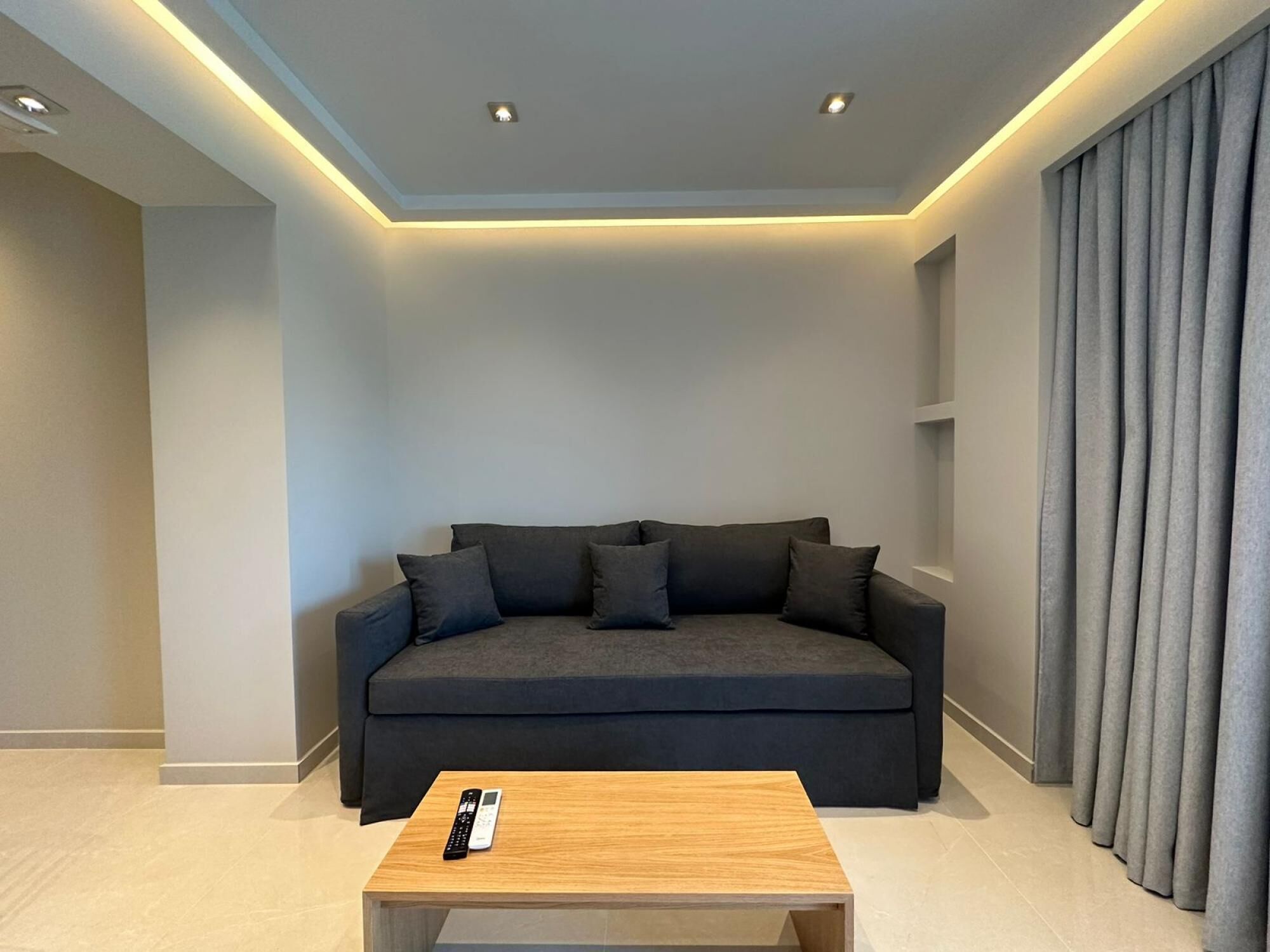 A modern living room with a dark grey sofa, a wooden coffee table, and a remote control on it.