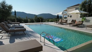 A swimming pool with lounge chairs, a floating pool toy, and a mountain view in the background. - Elpida Luxury Apartments & Suites (Lefkada)