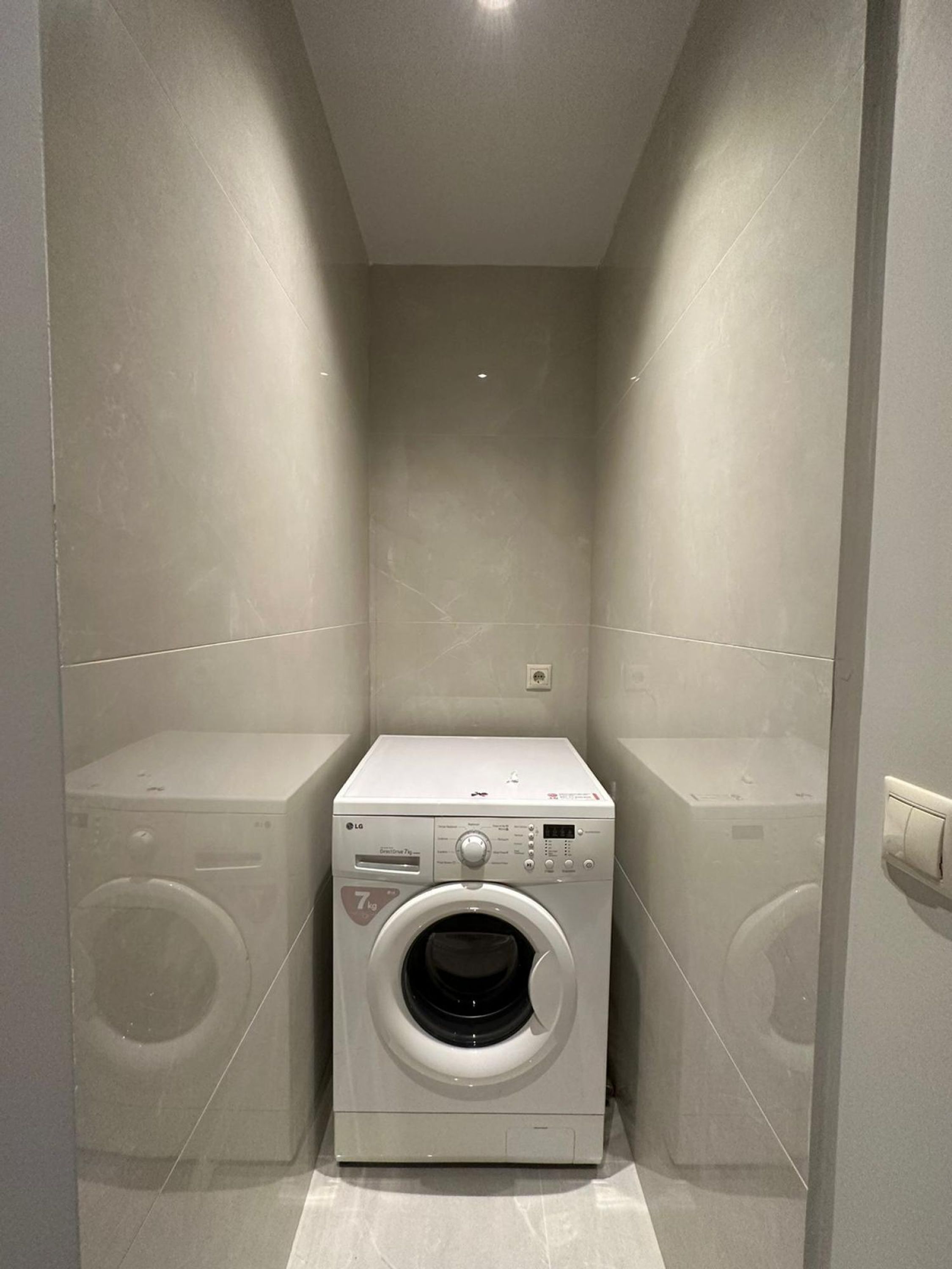 A compact laundry room with a front-loading washing machine, a dryer, and a small shelf.