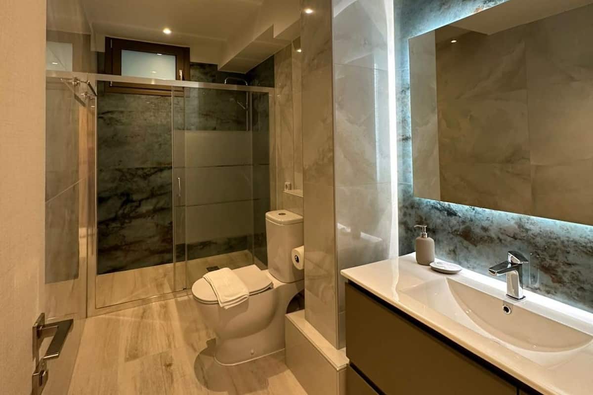 Une salle de bain moderne dotée d’une douche à parois de verre, de toilettes et d’un meuble-lavabo avec un grand miroir.