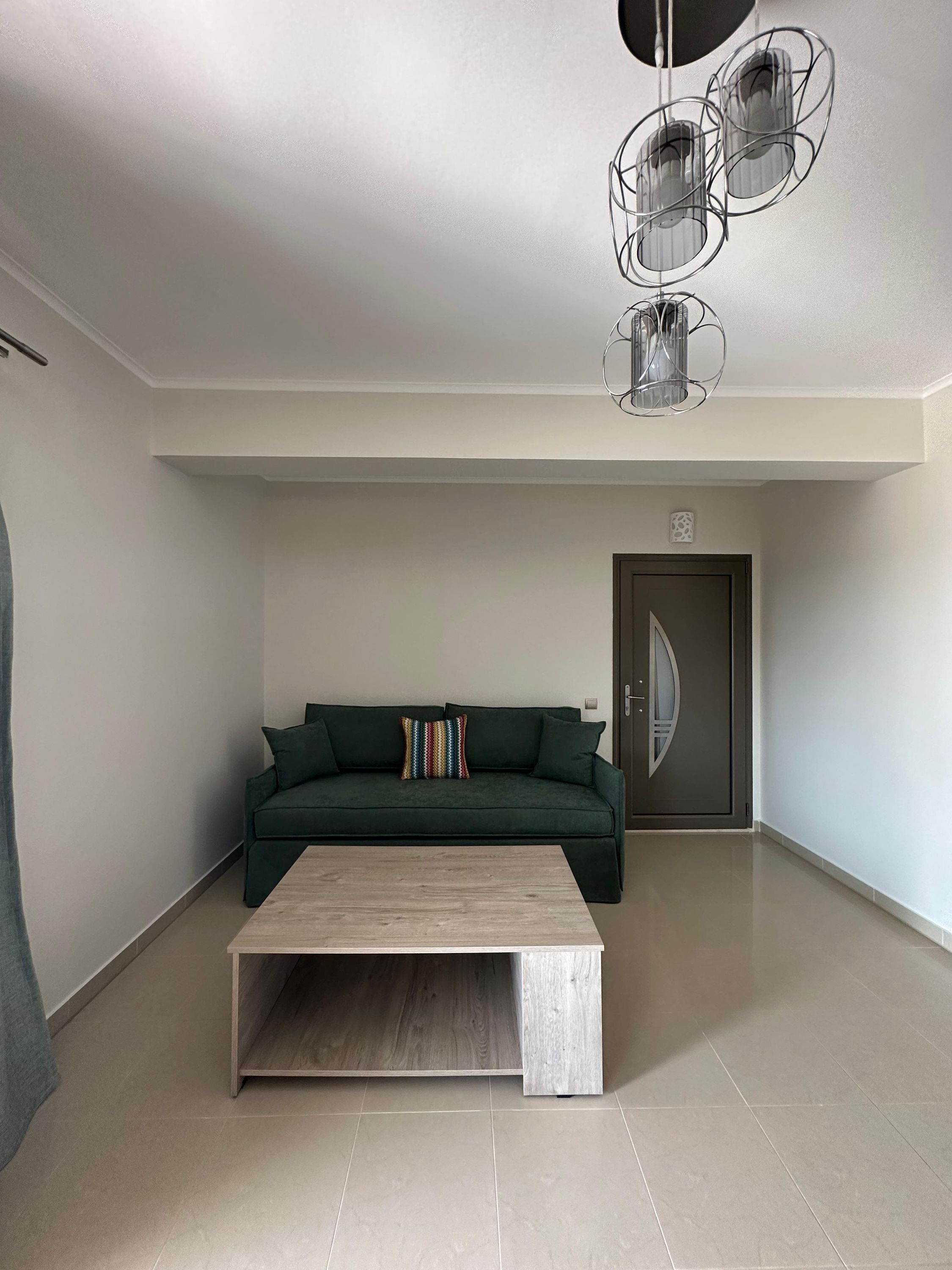 Ein geräumiges Wohnzimmer mit einem grünen Sofa, einem Holztisch und einer modernen Kronleuchter.