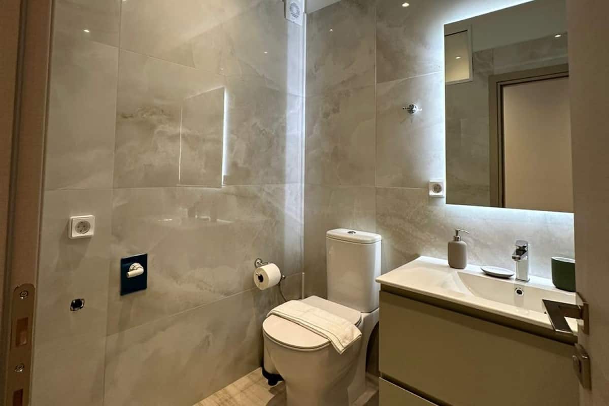 Une salle de bain moderne avec des murs en marbre, des toilettes, un lavabo et un miroir.