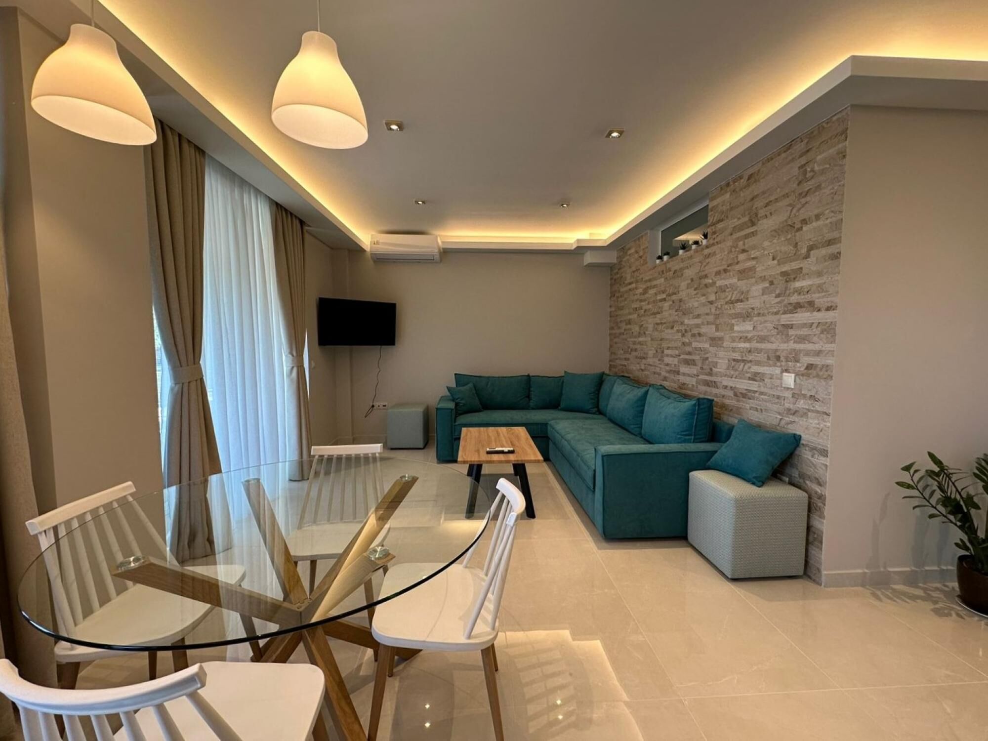 A modern living room with a glass dining table, teal sofa, and a stone accent wall.
