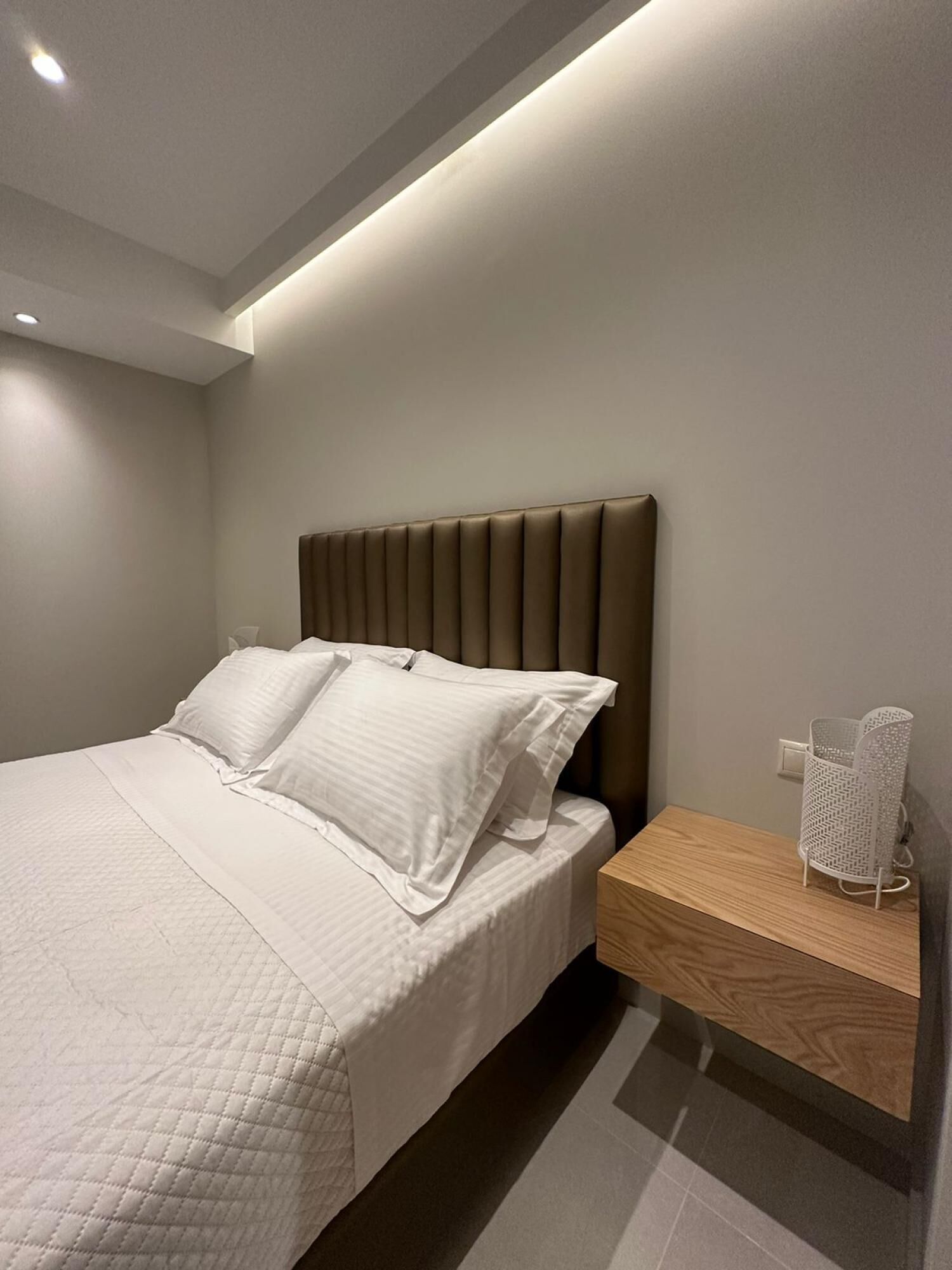 A modern bedroom with a bed, a nightstand, and a wall-mounted lamp.