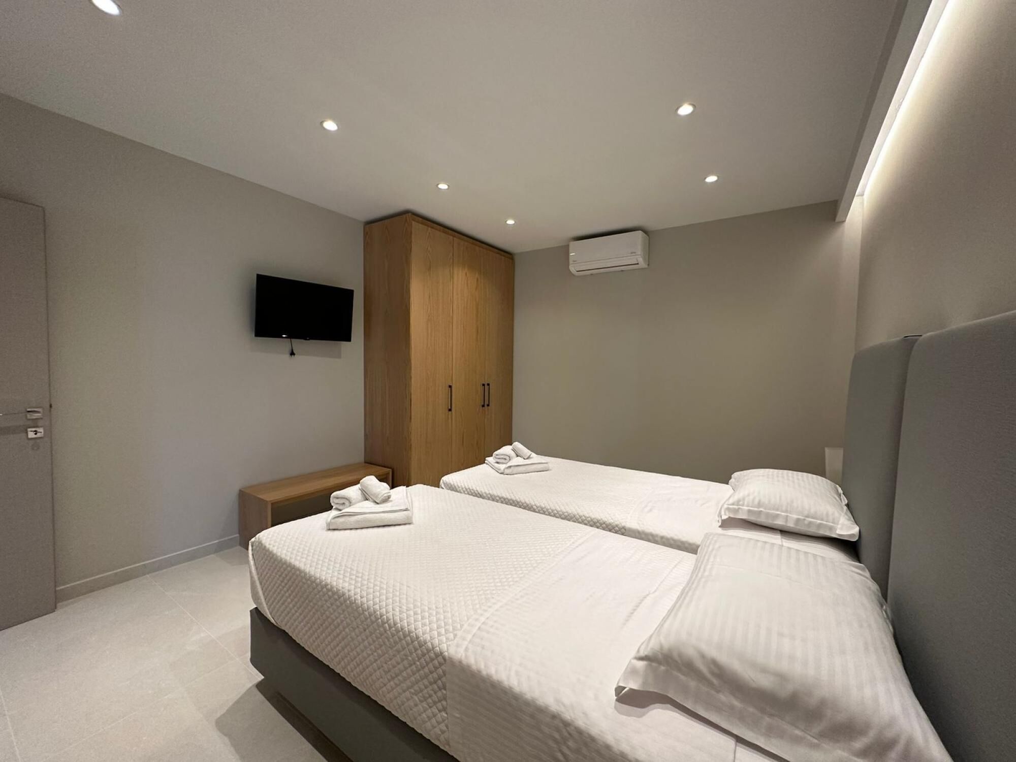 A modern bedroom with two beds, a TV mounted on the wall, and a wooden wardrobe.