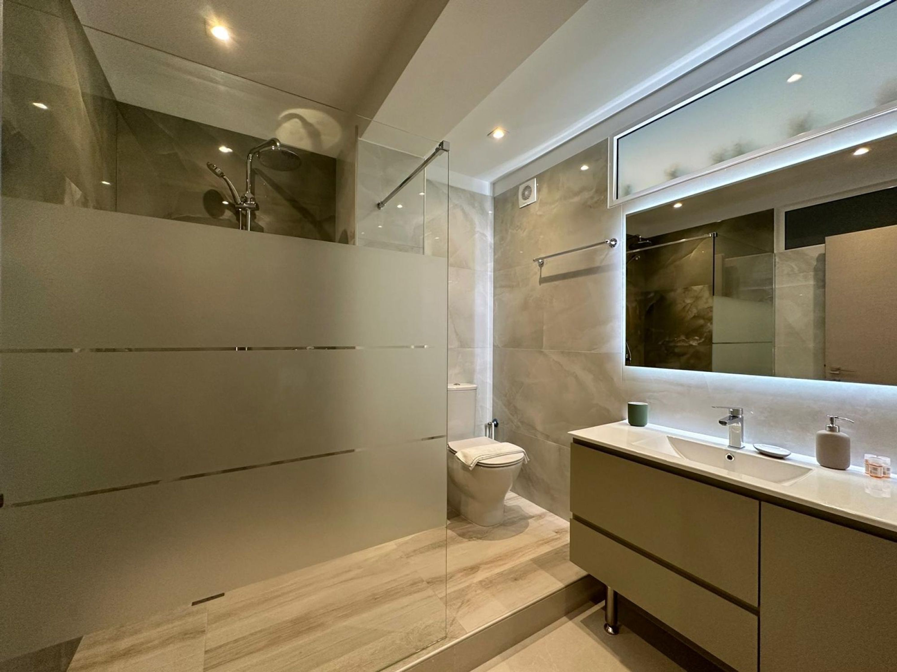 Ein modernes Badezimmer mit Glasdusche, Toilette und Waschtisch mit großem Spiegel.