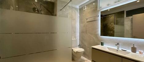 A modern bathroom with a glass shower enclosure, a toilet, and a vanity with a large mirror.