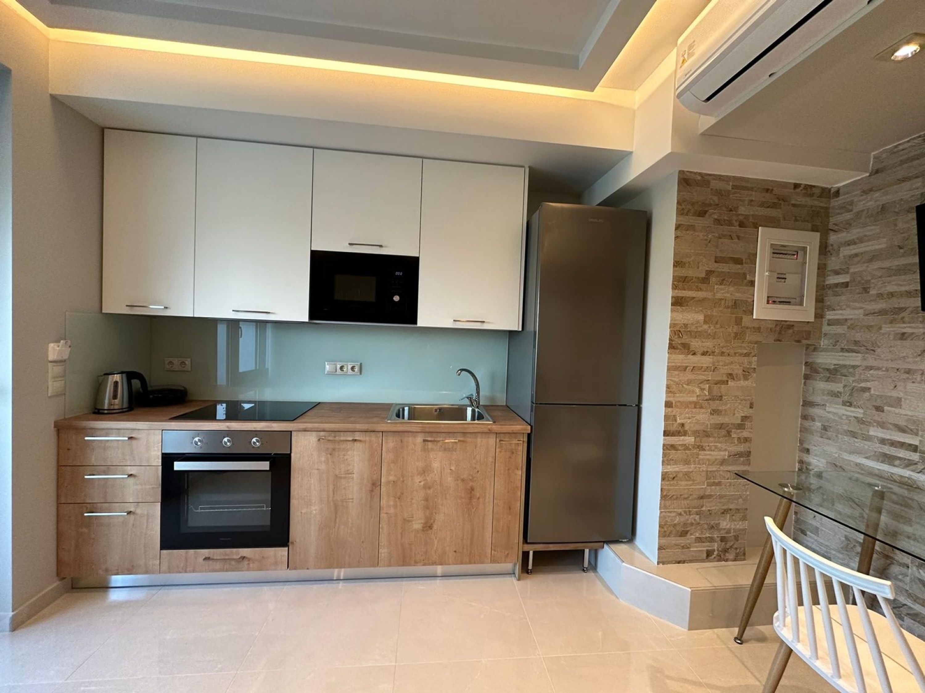 Una cocina moderna con armarios blancos, un microondas negro, un refrigerador de acero inoxidable y una encimera de madera.