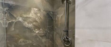 A modern shower with a glass enclosure, marble walls, and a wooden floor.