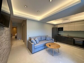 A modern living room with a sofa, a coffee table, and a kitchen area with appliances. - Elpida Luxury Apartments & Suites (Lefkada)