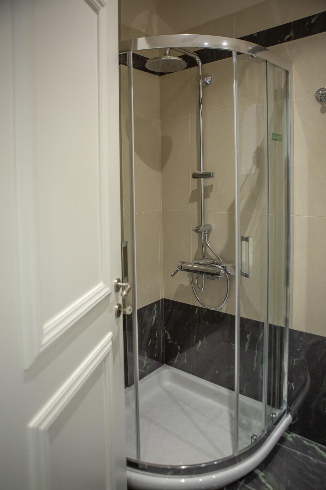 A glass-enclosed shower stall with a handheld showerhead and a handheld faucet.